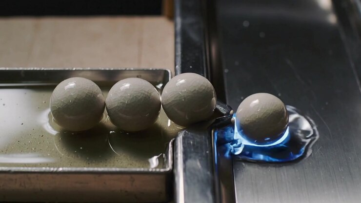 Esfera mais à direita se deslocando e rolando da borda metálica para uma abertura iluminada em azul no canal, empurrando a vizinha.