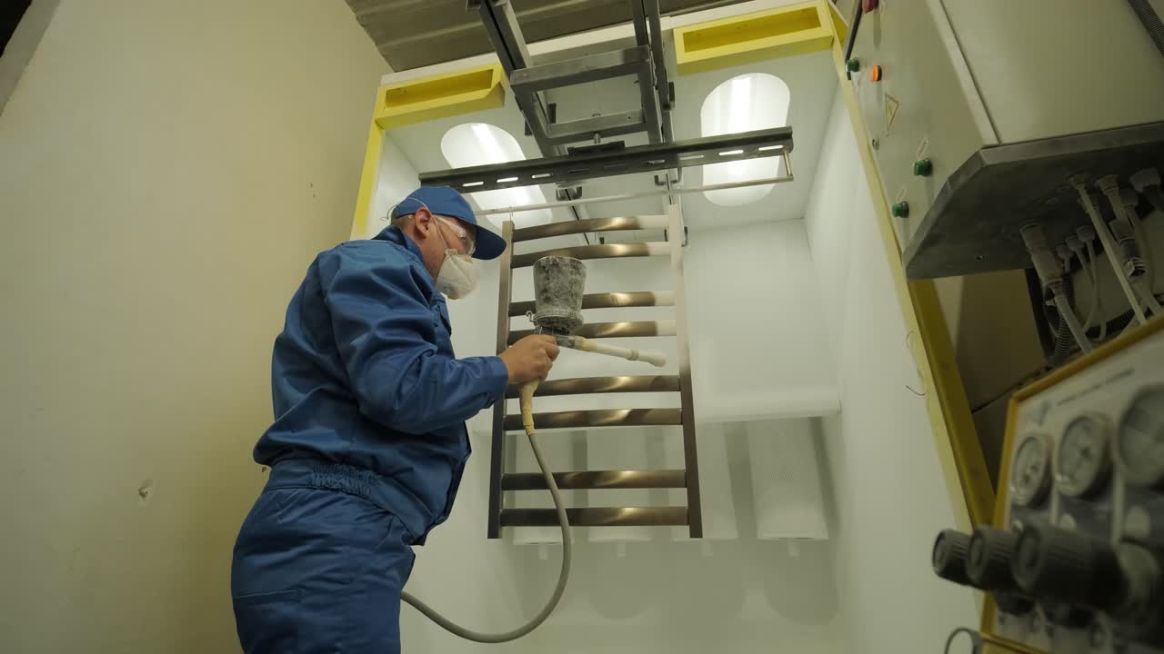 A worker paints a stainless steel metal structure with an airbrush spray gun. Dry painting method.