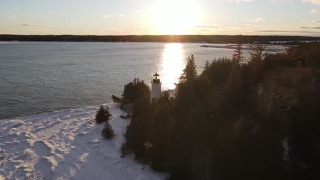 old presque isle lighthouse in michigan during the winter with a sunset