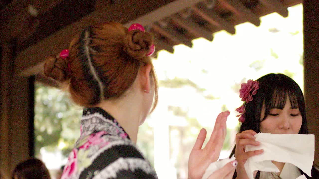 Primo piano di due donne in yukata floreali che usano salviette all'ingresso di un tempio giapponese.