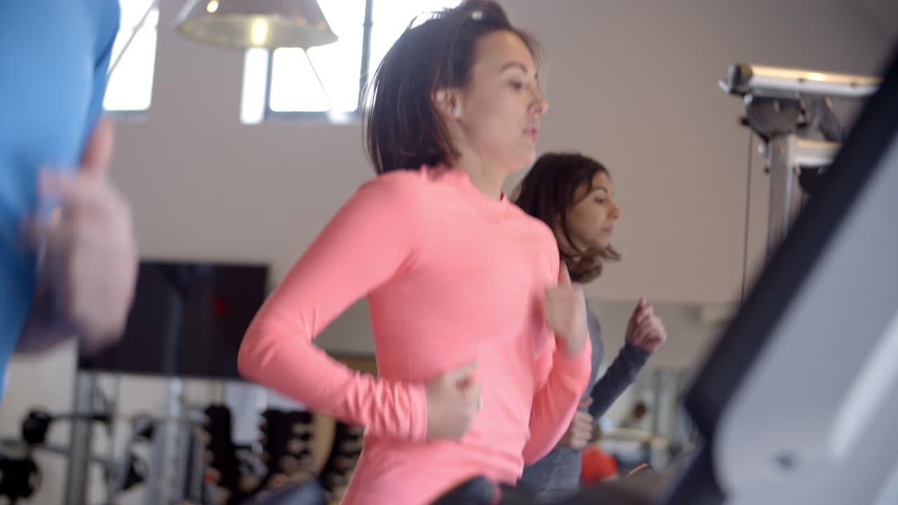 mujer y dos adultos jóvenes corriendo en cintas de correr en un gimnasio