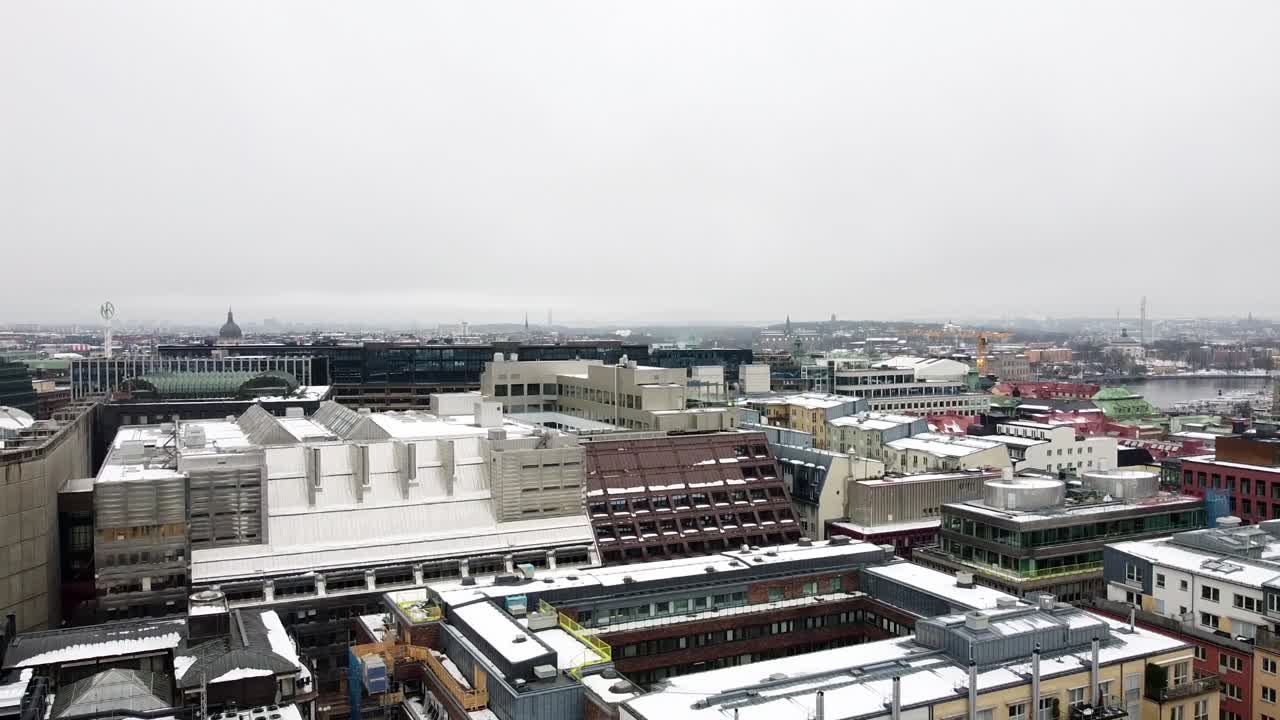 드론은 회색 구름이 많은 날 지붕에 눈이 있는 산업 아파트와 사무실을 드러내기 위해 아래로 기울어 올라갑니다.