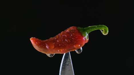 red pepper on knife against black background - close up