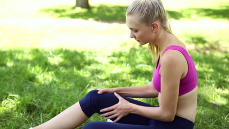 Injured-fit-blonde-touching-her-knee-on-the-grass