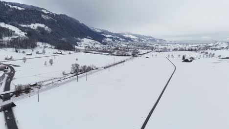 Drone-shot-showing-cloudy-day-in-winter-season,-with-small-village-and-snow-covered-fields-in-Switzerland