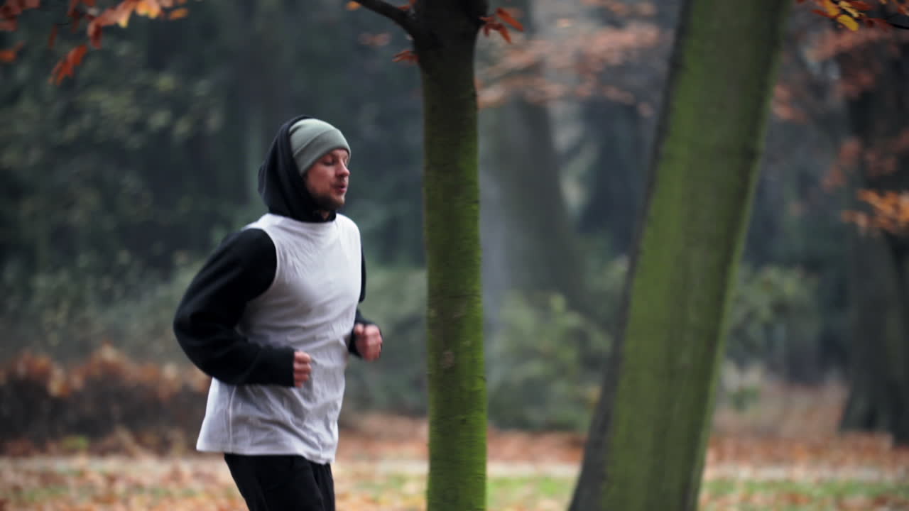 Pria Berhoodie Berlari Melintasi Hutan Musim Gugur