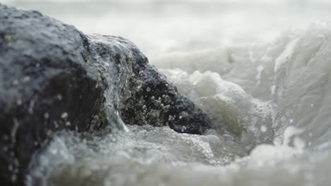 ocean waves crashing over barnacle covered rock on beach in slow motion