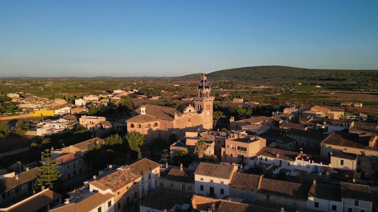 Veduta aerea di Santa Maria del Camí, una pittoresca cittadina a Maiorca, Spagna, che mette in risalto la chiesa prominente e l'architettura tradizionale, immersa nel caldo bagliore della luce dorata del tramonto.