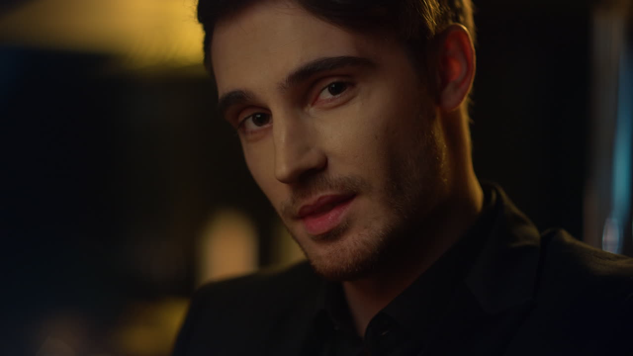 un chico encantador levantando las cejas en un fondo oscuro. un hombre guapo sonriendo en el interior.