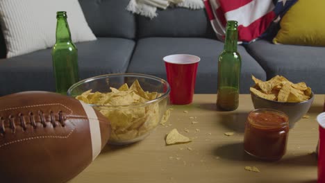 sala de estar en casa de la persona que ve un partido de fútbol americano en la televisión con bebidas, bocadillos y pelota