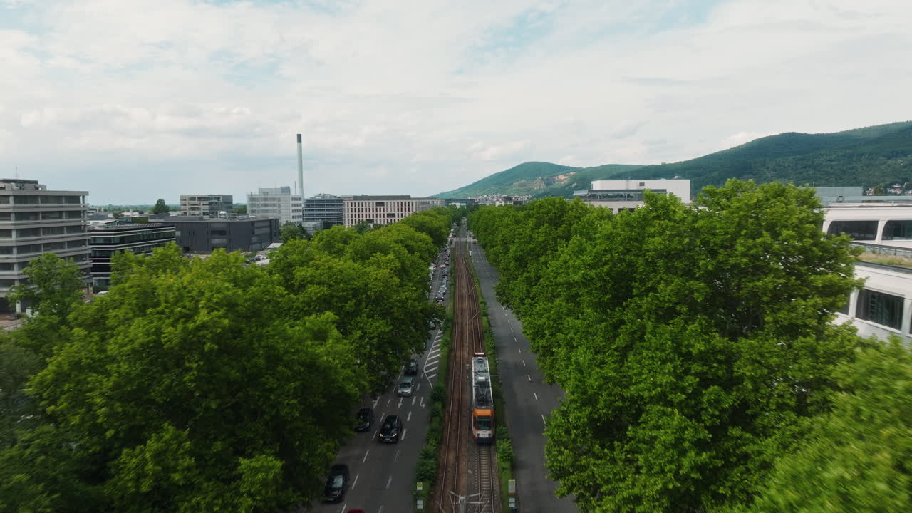 Drone tracking above treetops following city tram with cars and hills beyond