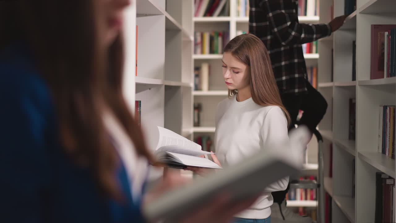 Una donna legge un libro mentre visita una biblioteca pubblica. Uno studente serio sfoglia le pagine di un libro di testo, lavorando con i compagni nella sezione di letteratura. Processo di studio