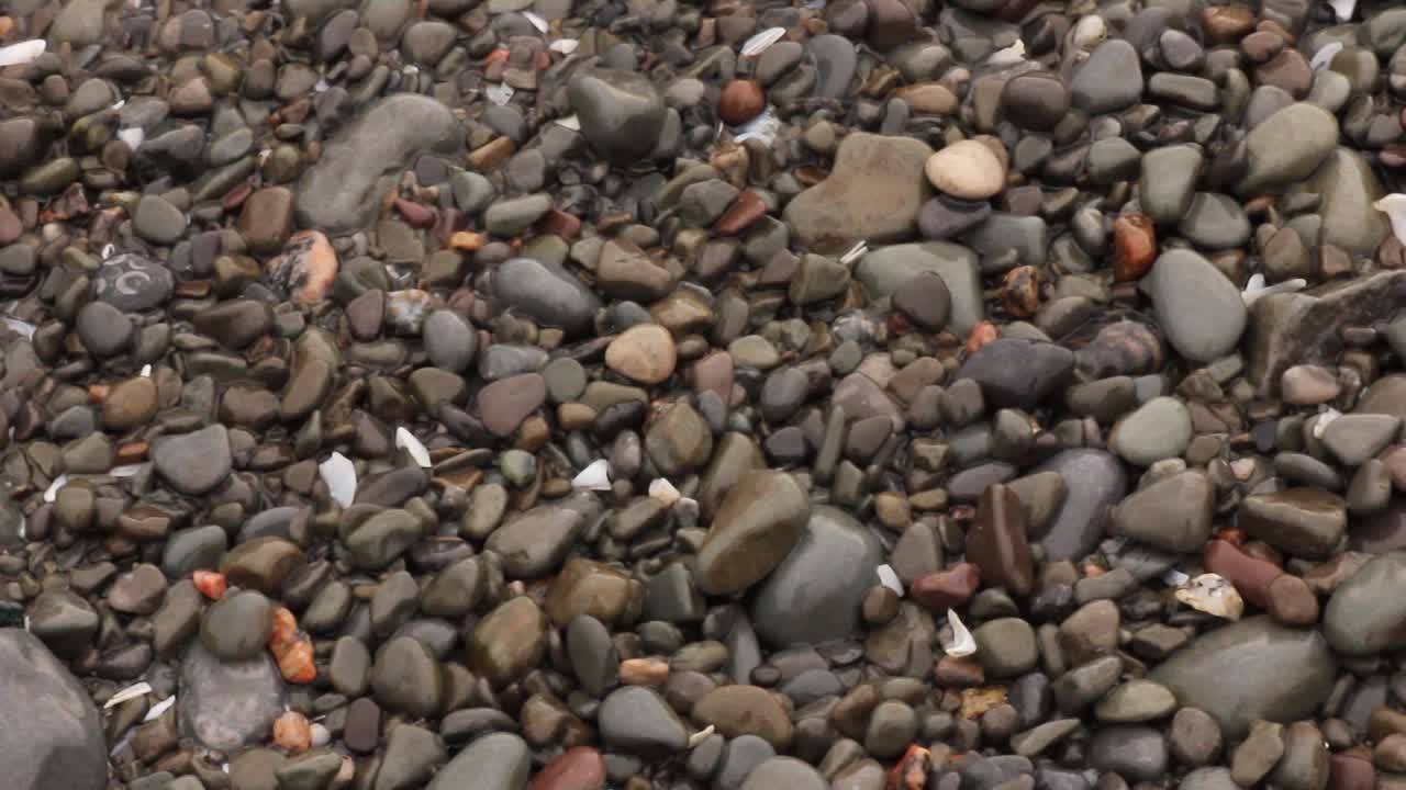 Pedras na praia sendo movidas pelas ondas na costa.