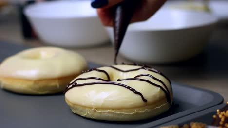 Close-up-of-a-woman's-hand-decorating-a-donut-while-baking-them,-dessert-and-bakery-pastry-concept