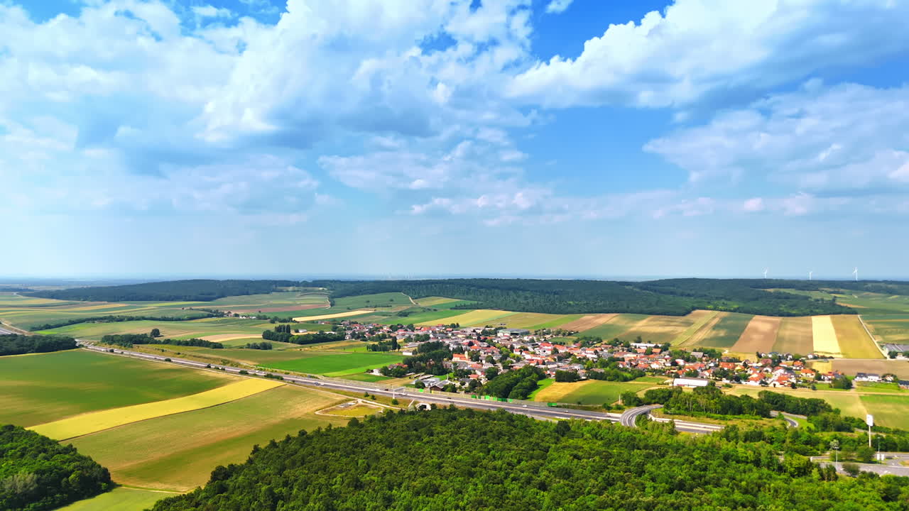 Vibrant landscape view of rural village. Aerial view showcases a tranquil rural village surrounded by fields and forests under a bright blue sky with clouds