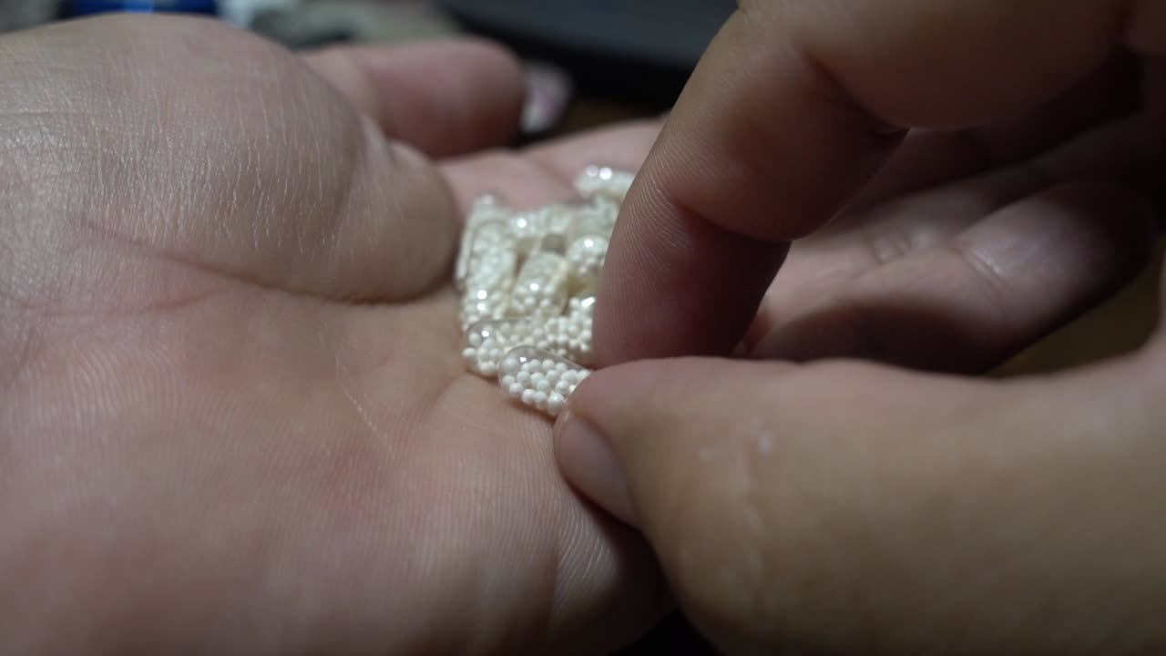verter varias cápsulas medicinales transparentes con pellets en el interior en una mano