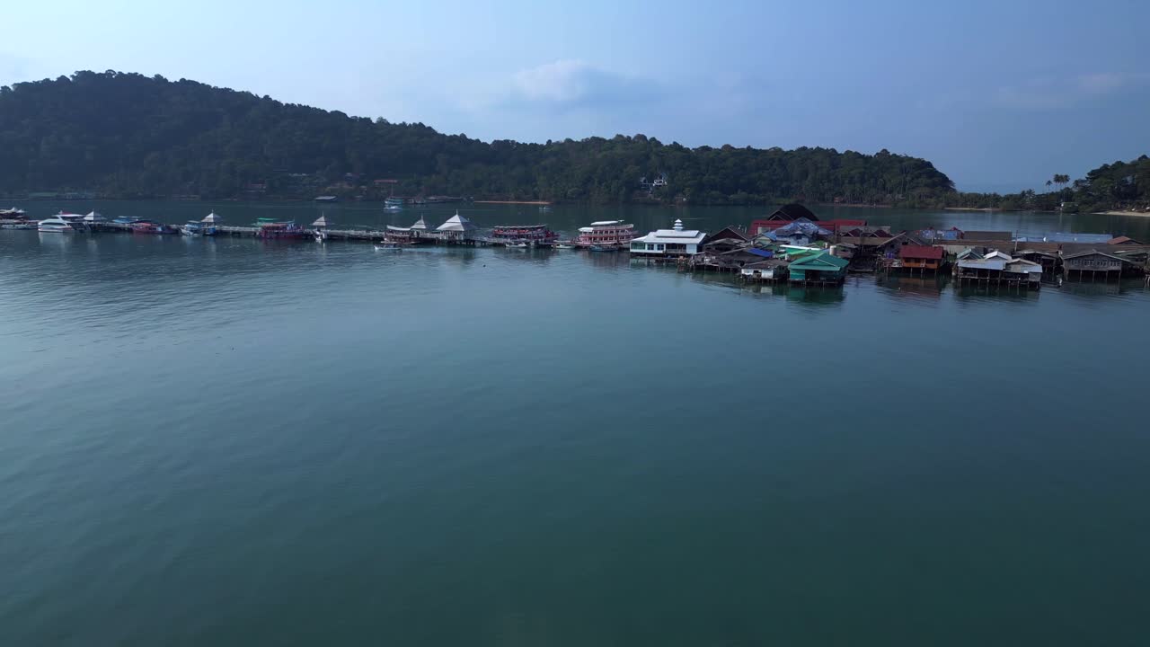Bang Bao Pier floating village in Koh Chang island, Thailand, showing colorful houses and boats sailing in turquoise water. Fantastic aerial view flight fly push forward drone