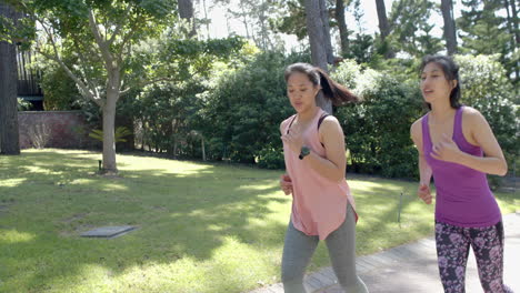 happy asian female friends running in garden on sunny day, slow motion