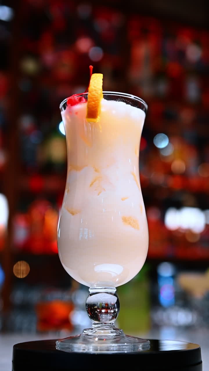 Creamy citrus cocktail glass. A creamy citrus drink with ice is served in a tall curved glass at the bar