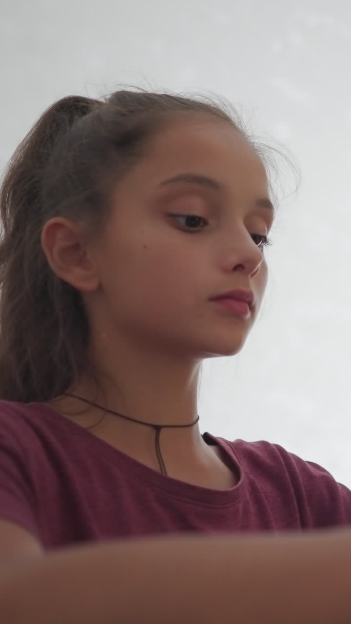 Primer plano de un niño escribiendo con un bolígrafo que toca a una niña que lleva una pulsera de cuerda roja mientras escribe en un portátil; ella se detiene para echar un vistazo a su trabajo, mostrando curiosidad e interés durante un momento de estudio compartido en casa.