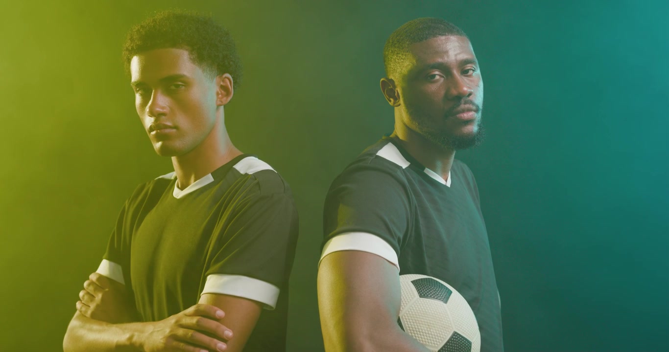 Companheiros de equipe africanos com uniformes pretos posando na grama sintética, a câmera subindo, segurando uma bola de futebol para promoção.