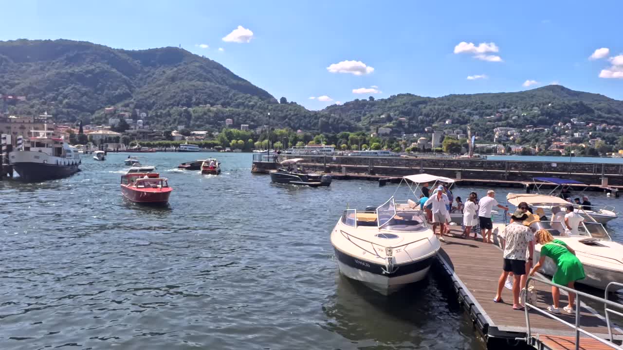 A scenic view of the pier in Lake Como with stationary boats and the hills behind in Lombardy, Italy