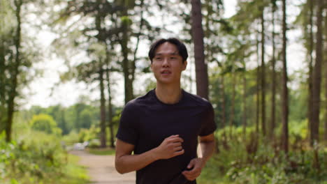 mid adult man exercising doing work out outdoors running along track through forest towards camera wearing sports clothing