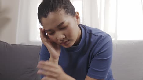 asian woman wearing a blue shirt sitting on a sofa feeling very headache