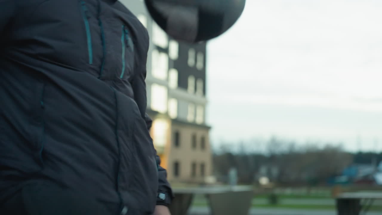 도시 스포츠 경기장에서 훈련하는 동안 축구 공을 조롱하는 운동 선수의 클로즈업, 조명 된 주거 건물과 야외 피트니스 장비의 흐릿한 배경으로 통제를 강조합니다.