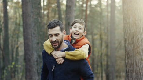 vista de cerca de un apuesto hombre caucásico que le da a su pequeño hijo un paseo a cuestas en el bosque