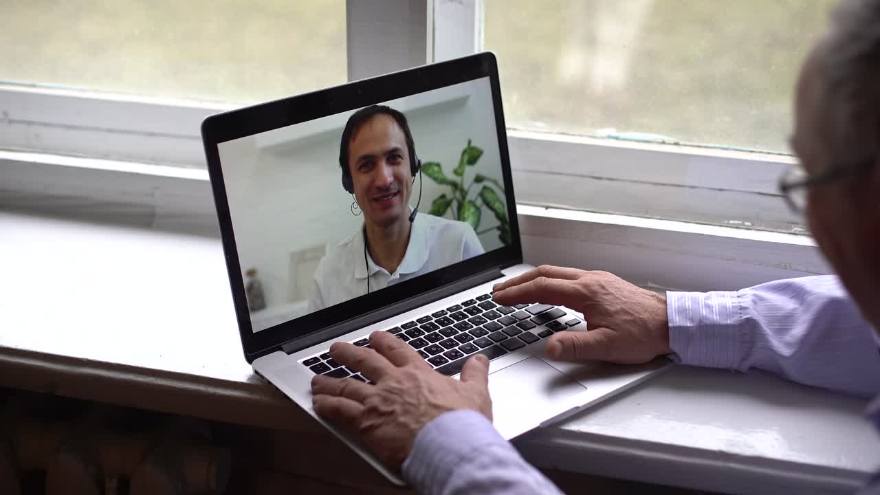 modern medicine, elderly man communicates with doctor online via video communication using laptop while sitting at home at table during quarantine isolation