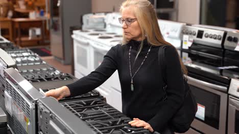 Pretty-mature-blonde-woman-looking-at-the-features-and-benefits-of-a-gas-stove-in-a-kitchen-appliance-store