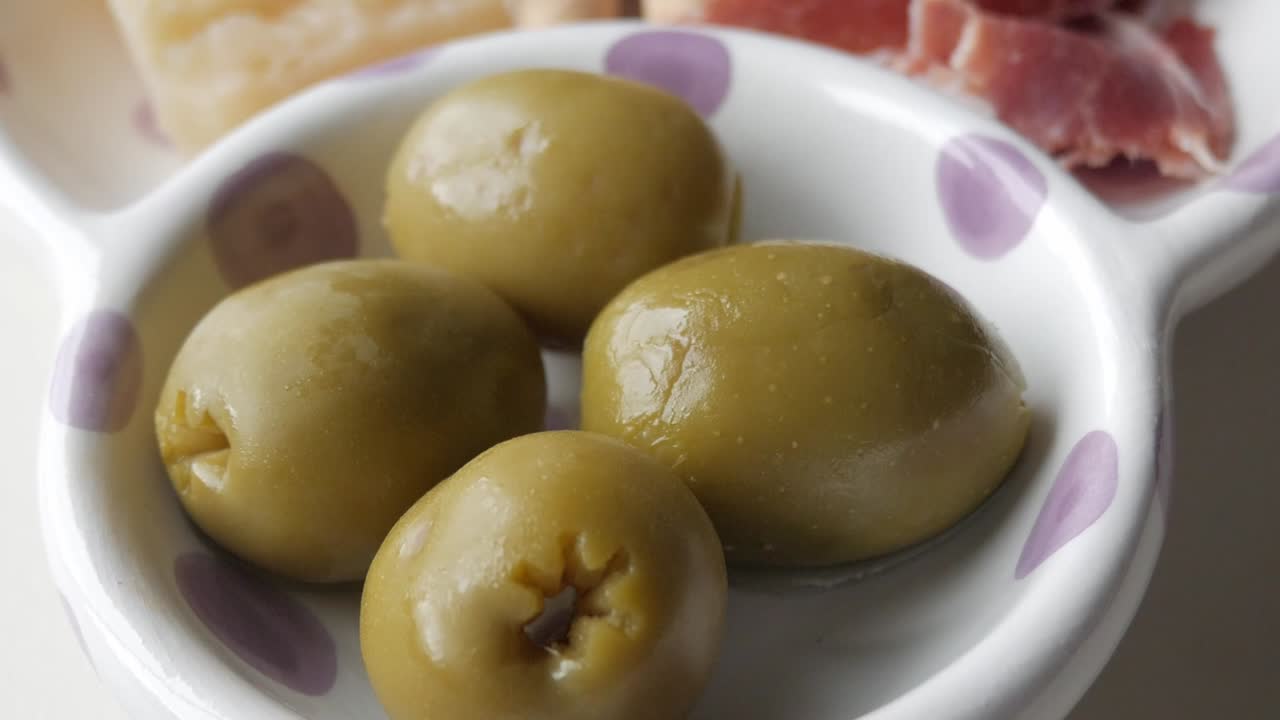 Olives in a bowl, part of a traditional tapas spread with cheese, jamon, and colines