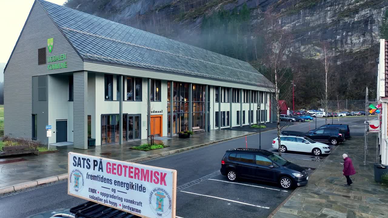 Aerial rises over protest car from Norges Miljovernforbund near municipality house in Modalen, Norway, advocating geothermal energy over wind turbines