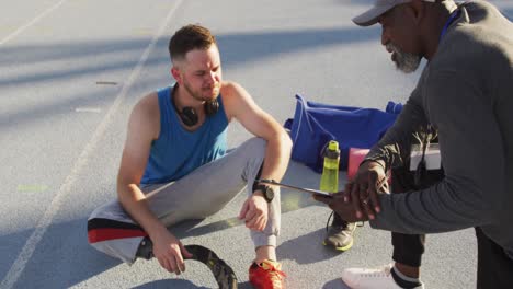 diverse male coach and disabled athlete with prosthetic leg talking during training session