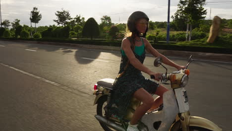 young caucasian woman with long blond hair cautiously riding a vintage style moped along the deserted roads of vietnam