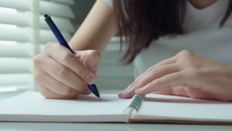 close up hand young female is writing notes and planning her schedule in living room at home.business woman holding pens and papers making notes in documents report on the table.