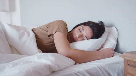 Woman-Asleep-In-Bed-Reaches-Out-To-Turn-Off-Alarm-Clock-On-Bedside-Table