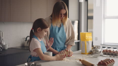 mother and little daughter are making dough in kitchen together woman is teaching her child to cook