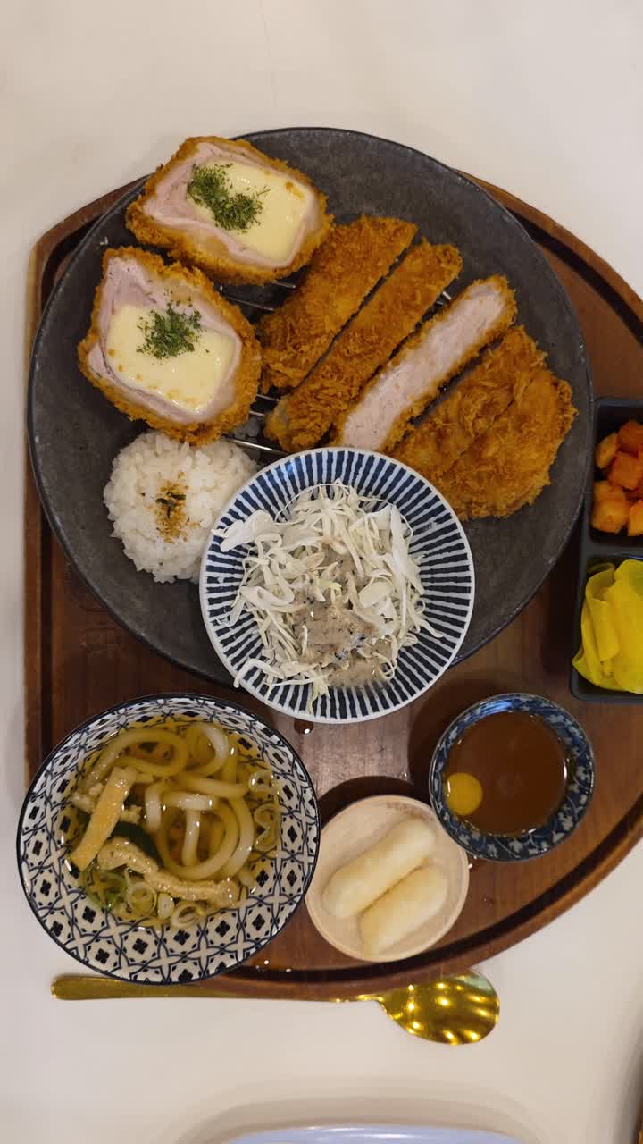 A well-presented Japanese tonkatsu meal set including breaded pork cutlet, cheese katsu, cabbage salad, steamed rice, udon noodle soup, dipping sauce, and light dessert