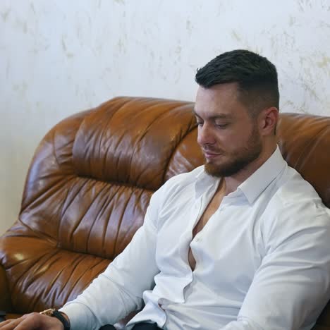 Handsome businessman with a laptop in hotel. Young bearded man is sitting on a comfortable sofa next to suitcase and working on a laptop at business trip