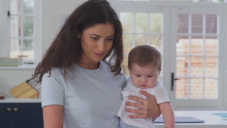 Close-Up-Of-Mother-With-Baby-Son-Working-From-Home-On-Laptop-In-Kitchen