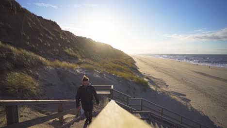 man going up wooden stairs on a beach in summer with a strong sun in the background