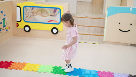 preschool 3-year-old girl walking on colorful bumpy texture tiles at indoor playroom