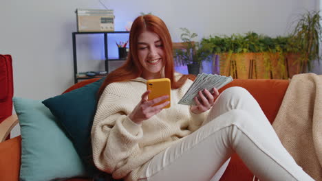 mujer joven sonriente feliz contando dinero en efectivo uso de teléfono inteligente ingresos ahorra lotería ganar presupuesto en casa