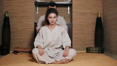 young male thai massagist is massaging young woman's back and shoulders sitting behind her