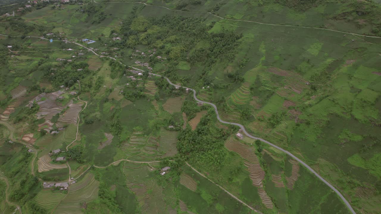 Aerial view of lush green rice terraces and a winding road in a mountainous rural landscape
