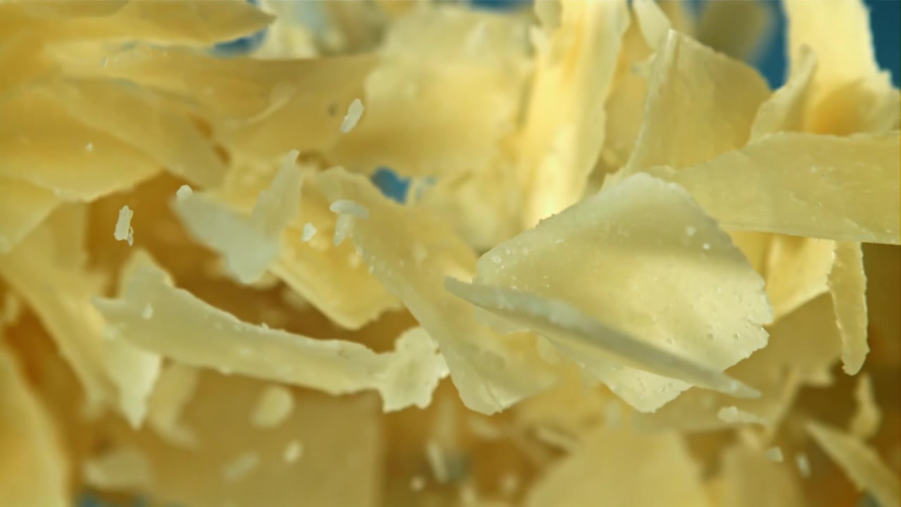 Copeaux de fromage Parmesan tombant au ralenti sur fond bleu