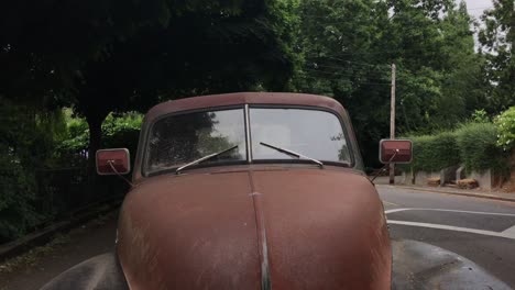 A-wide-shot-of-the-front-of-a-rusted-out-car-on-the-street