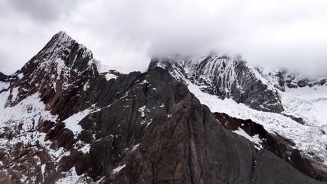 Cinematic aerial view of snowy Andes mountains in Peru with glaciers, rocky cliffs, and hidden blue alpine lake under misty clouds, dramatic landscape and natural travel destination